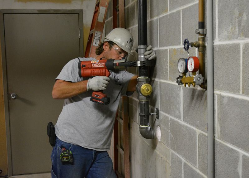 plumber repairing plumbing system on wall with power tools